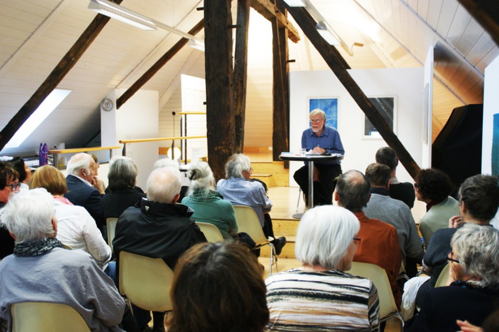 Erhard von Büren an einem Pult am Lesen vor Publikum